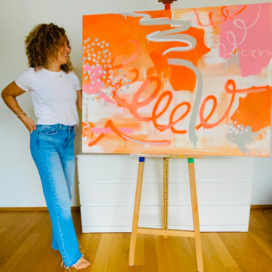 Handgemaltes Gemälde in Orange, Pink, Grau und Weiß stehend auf einer Staffelei zu Hause neben FLOR.