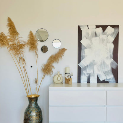 Ein braun weisses Bild stehen auf einer weissen Kommode mit Boho Dekoelementen von FLOR.